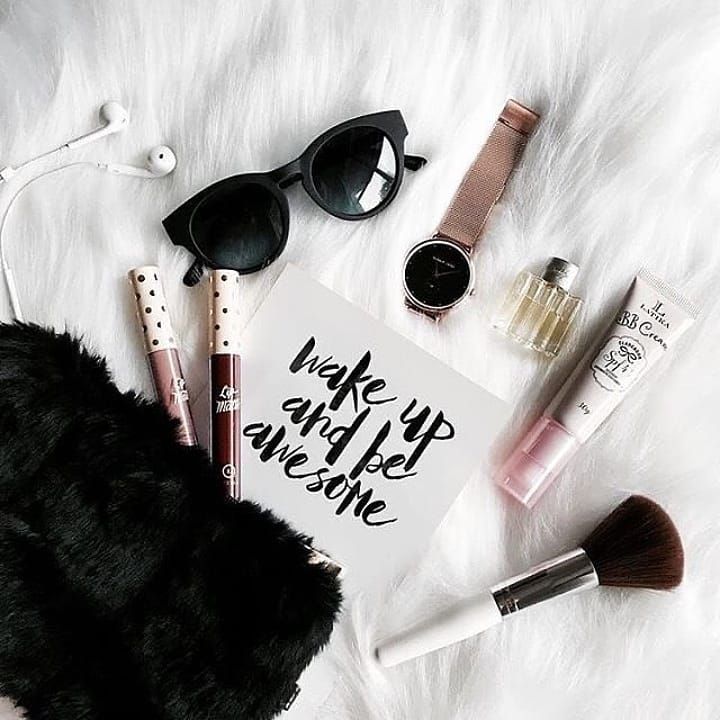 Flatlay of makeup essentials, sunglasses, BB cream, watch, and lifestyle accessories on a white fur background.”